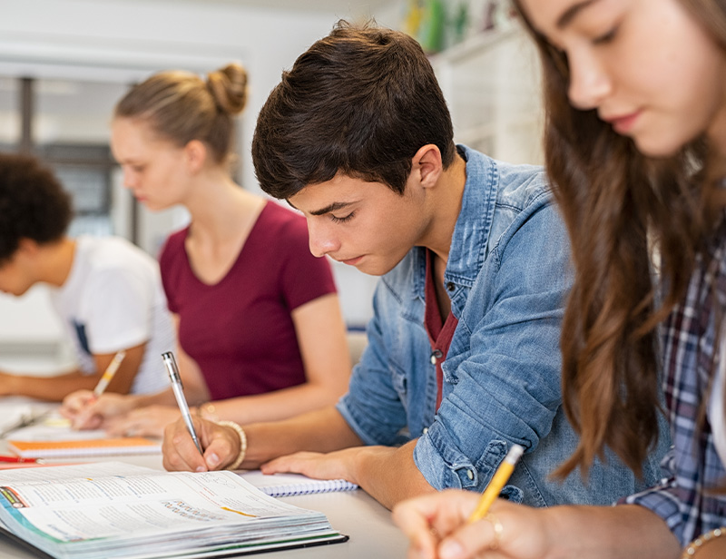 students studying together in classroom focused on notebooks and writing supplies engaged in collaborative learning and academic achievement