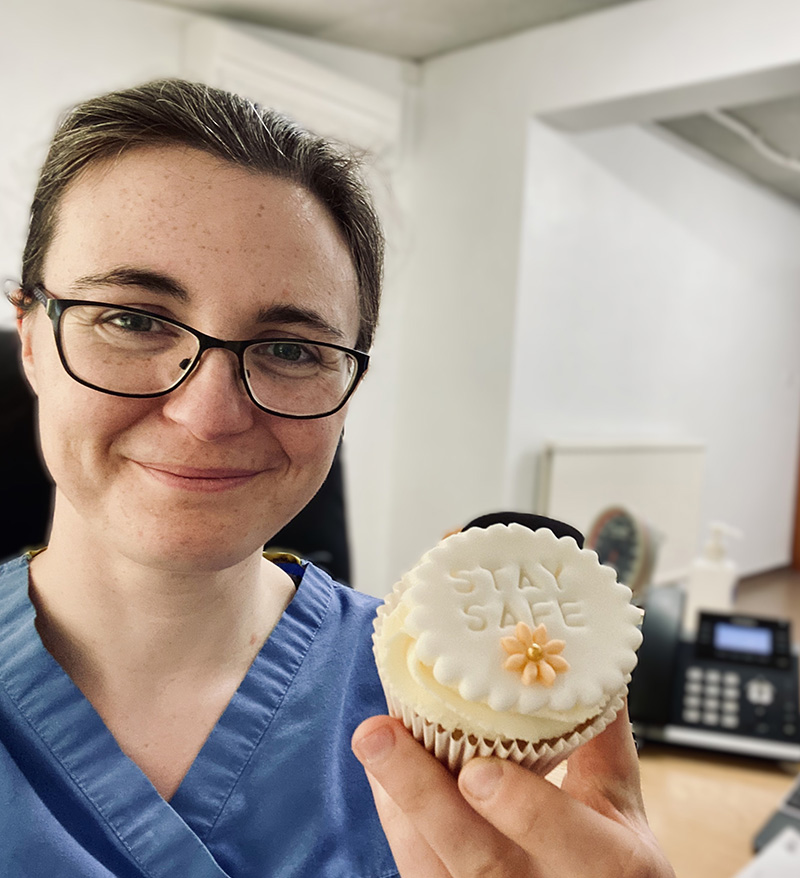 smiling woman in scrubs holding cupcake with stay safe decoration in a bright office environment five ways to stay safe in health